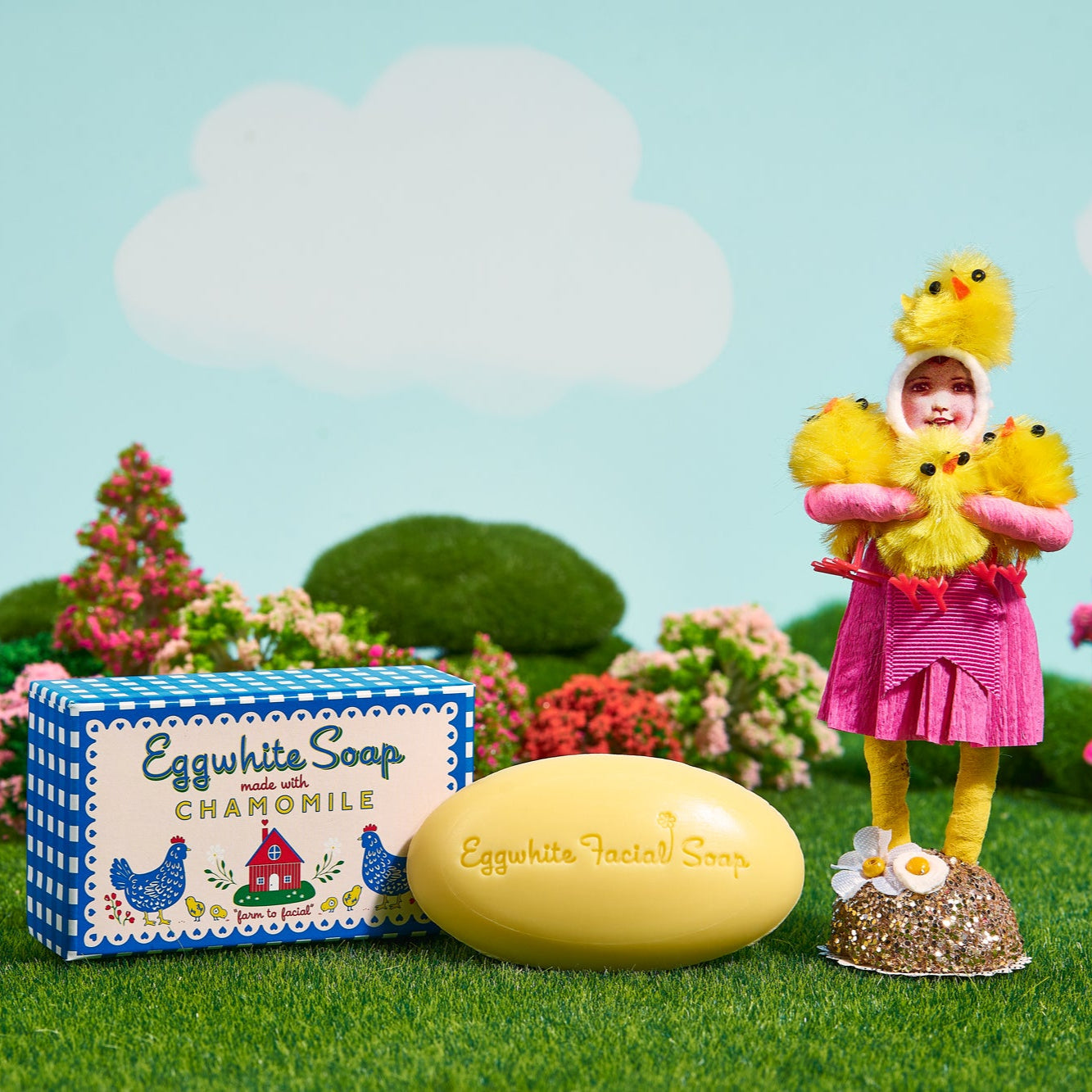 Eggwhite Soap product with a toy figure and small animal on a grassy field with flowers and sky background
