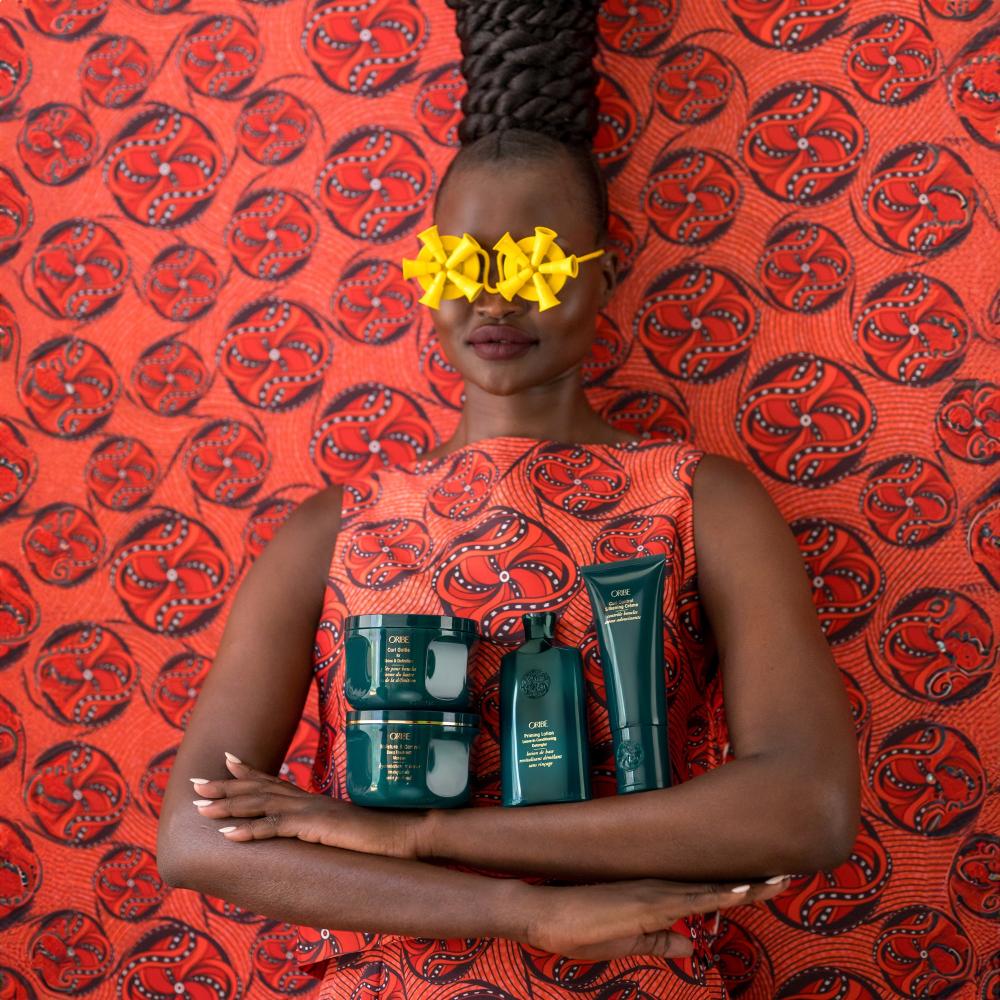 Model wearing orange print dress holding Moisture Control Set on a orange patterned backdrop  