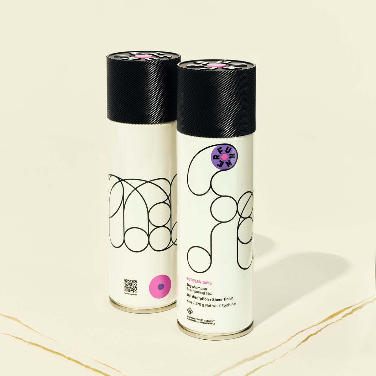 Two dry shampoo cans with black lids on a beige background