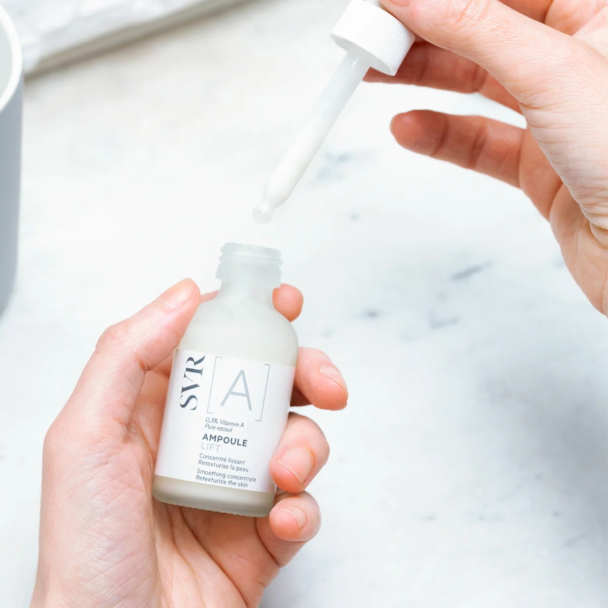 Person holding a SVR Ampoule bottle with a dropper over a marble surface