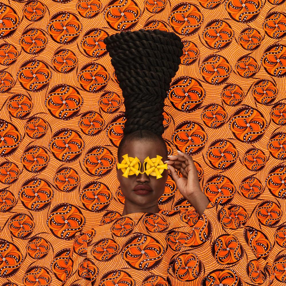 Women with yellow abstract glasses with orange dress on orange print backdrop 