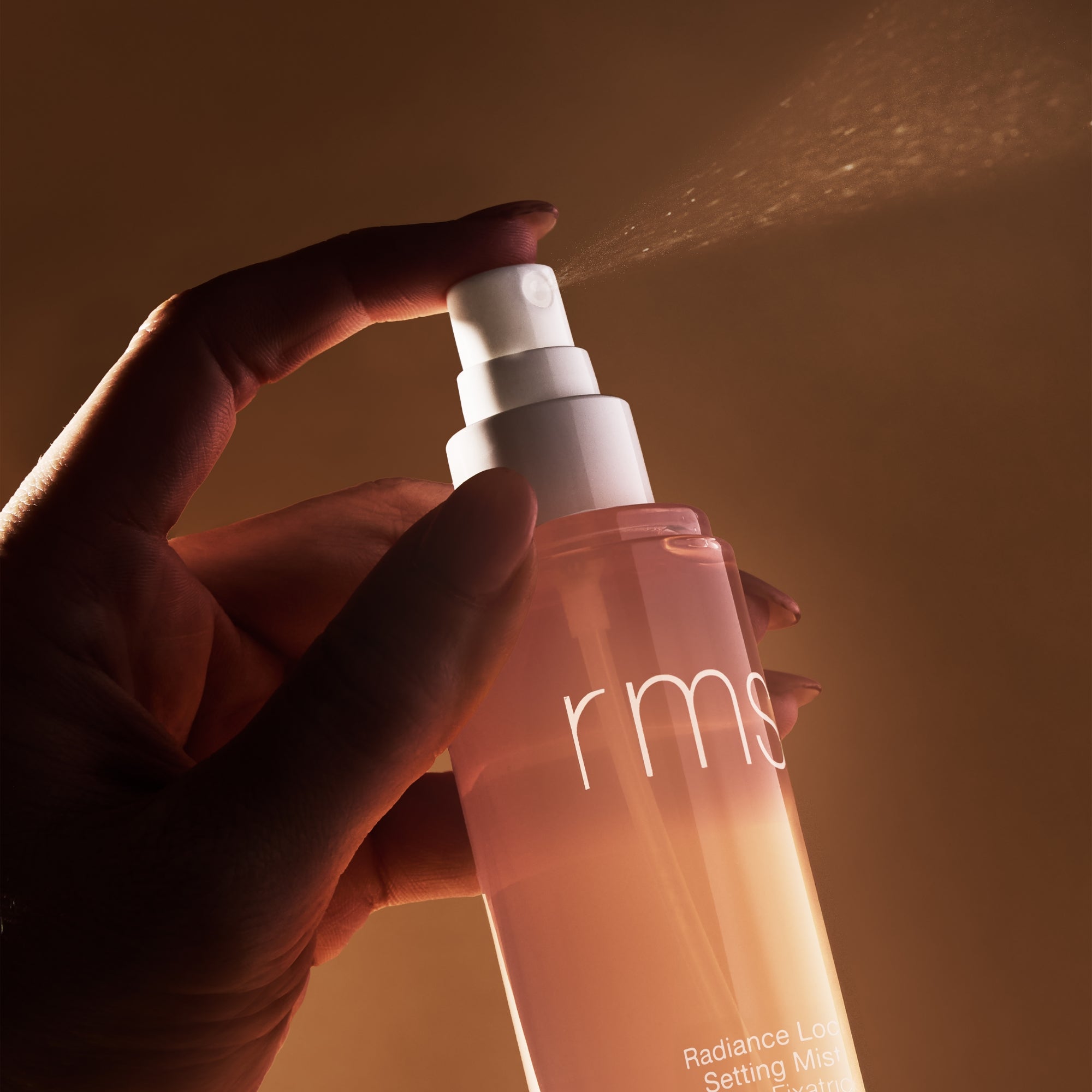 Hand holding a RMS beauty product with a warm, brownish background
