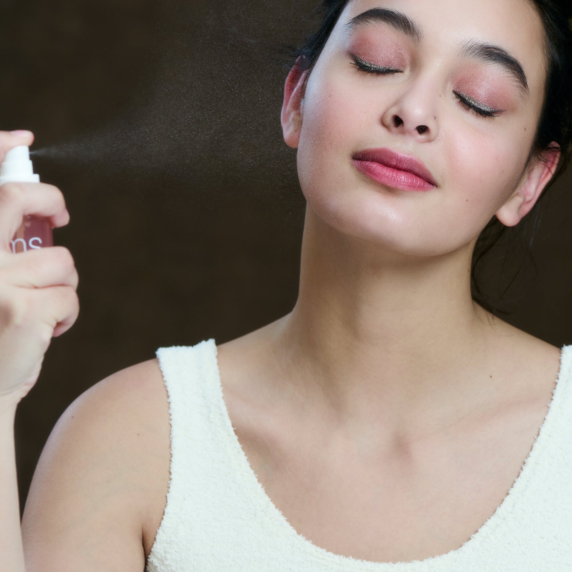 Woman applying a mist spray to her face with a blurred background