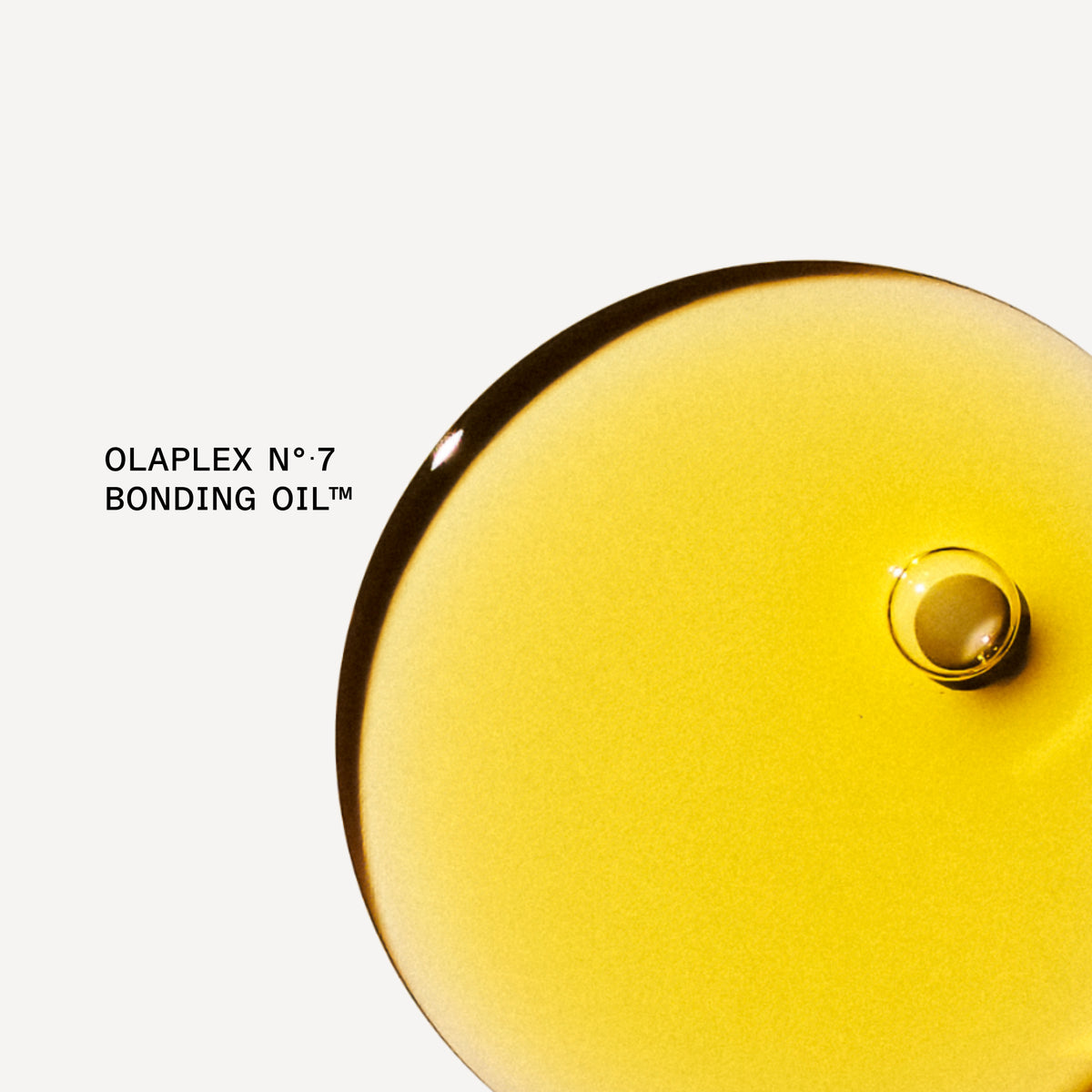 A close-up studio shot of a glossy, translucent golden-yellow liquid droplet on a light gray background, with the text 'OLAPLEX N°7 BONDING OIL™' printed to the left.