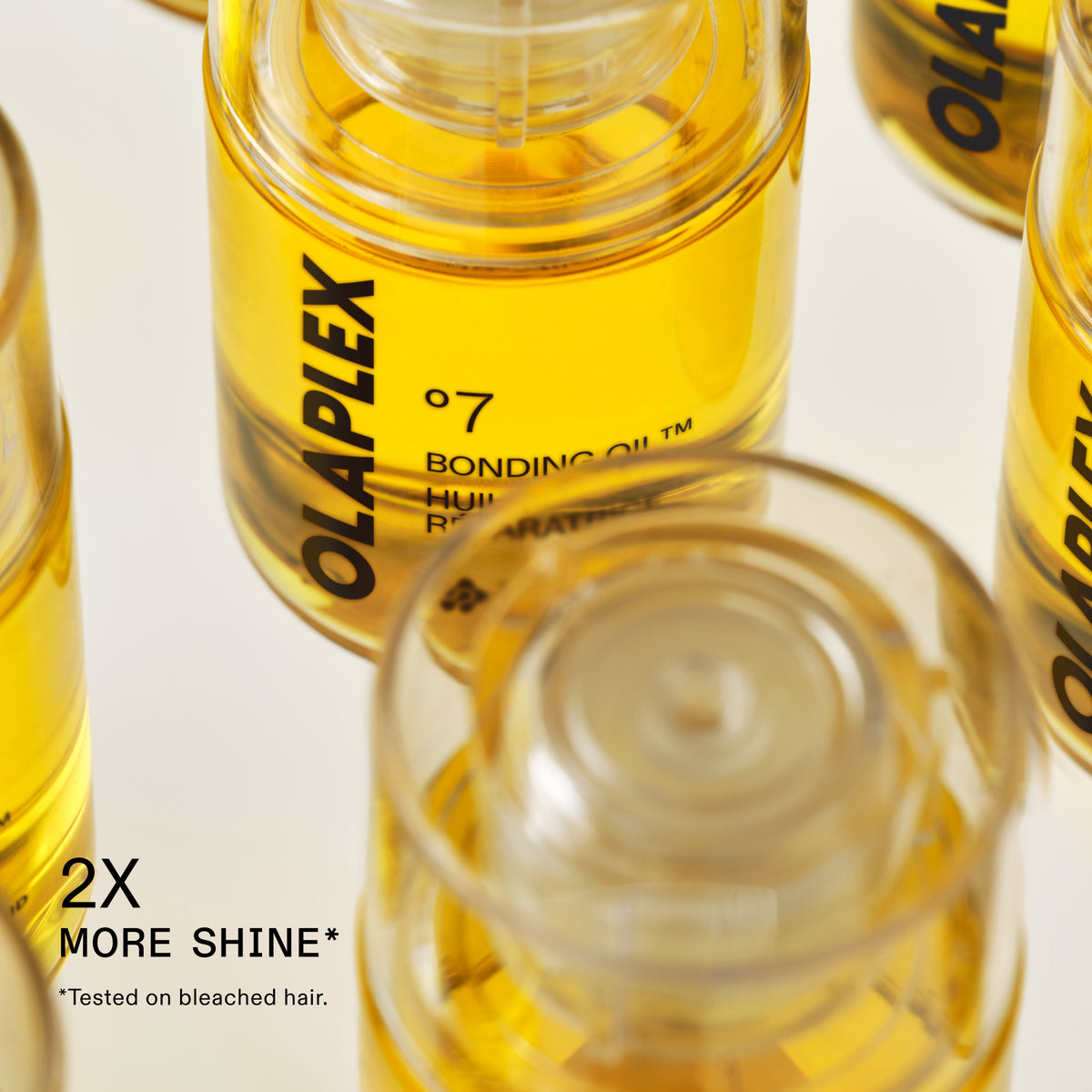 Several clear cylindrical bottles of Olaplex Bonding Oil filled with golden yellow liquid, arranged on a white background. One bottle is upright and clearly shows the black OLAPLEX branding and product text, while other bottles are cropped and in the foreground.