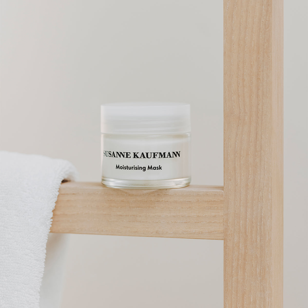 Jar of Susanne Kaufmann moisturizing mask on a wooden shelf with a white towel.