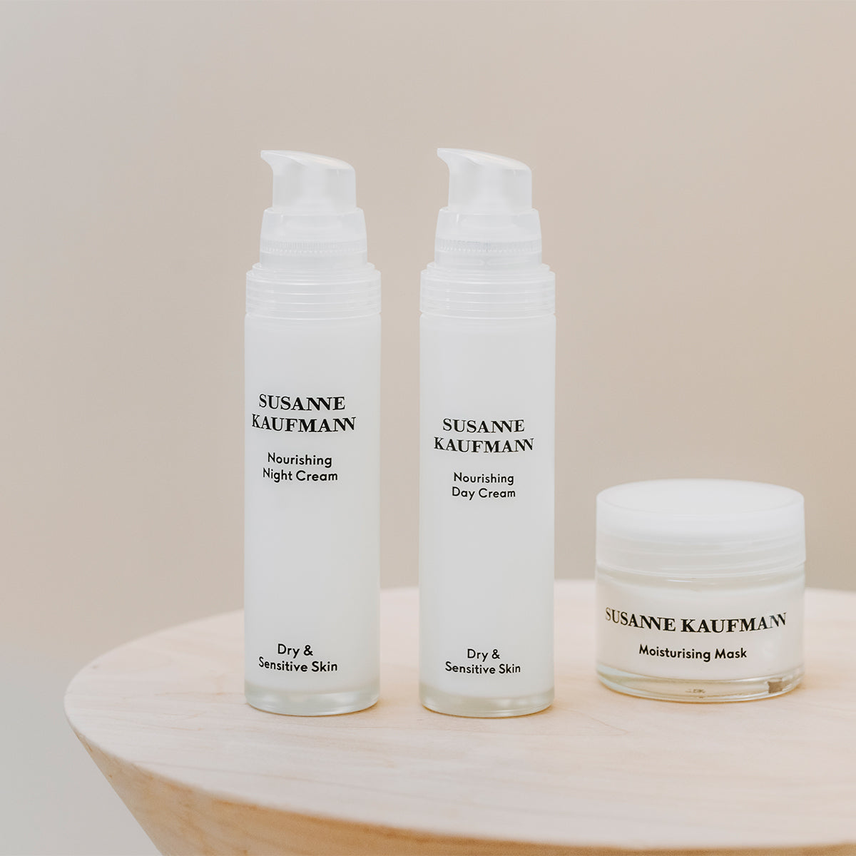 Three Susanne Kaufman skincare products on a wooden stand with a beige background
