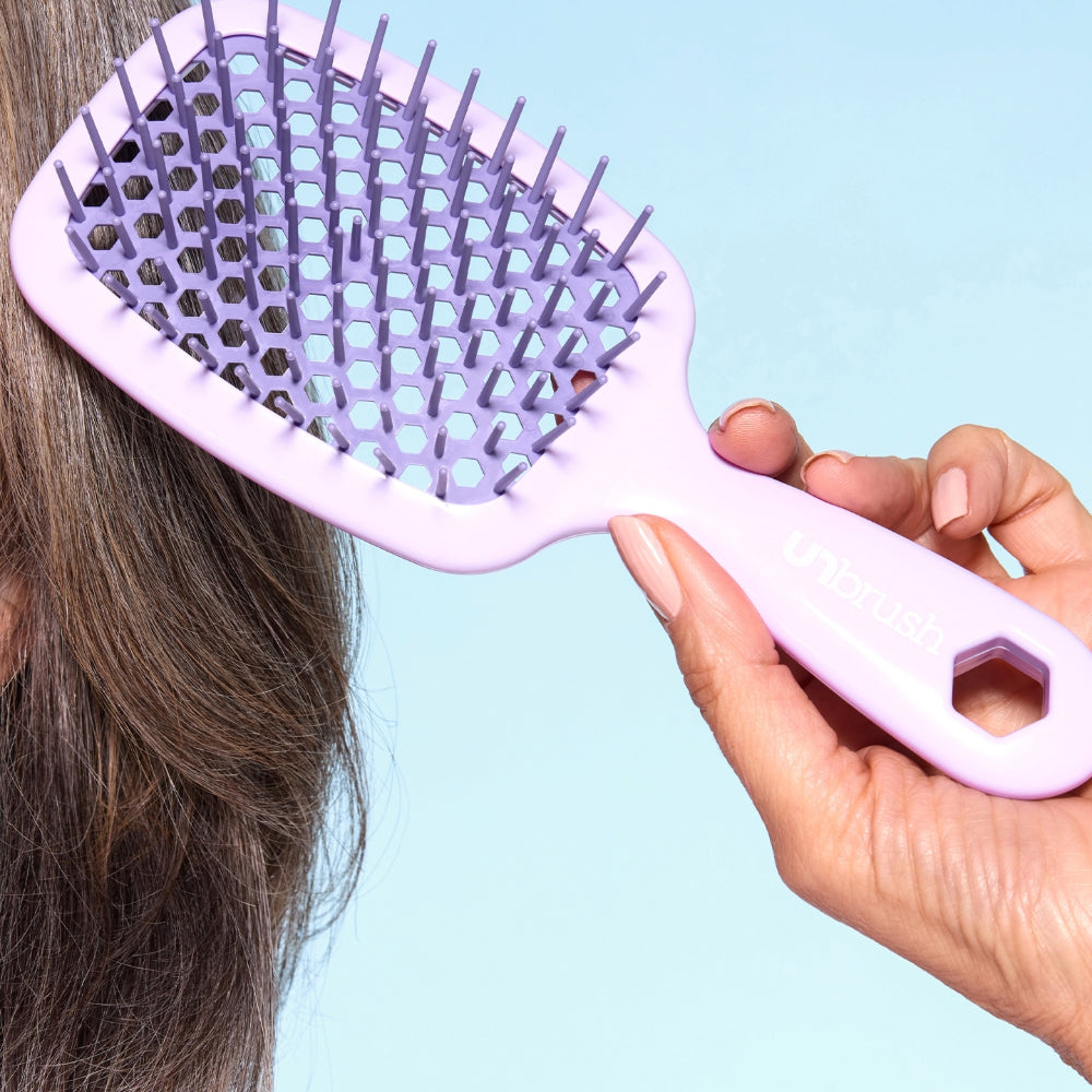 Person using a purple brush on their hair against a light blue background