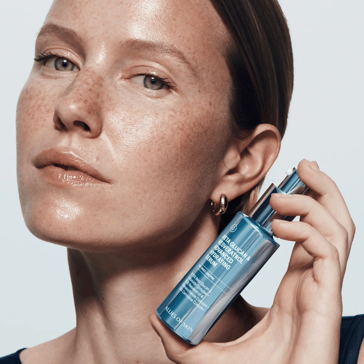 Woman holding a skincare product against a neutral background