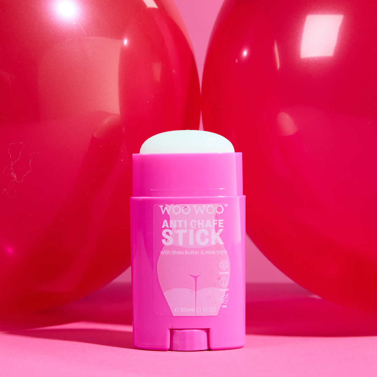A pink deodorant stick labeled 'WOO WOO ANTI CHAFÉ STICK' sits centered in front of two large glossy red spheres on a pink studio background.