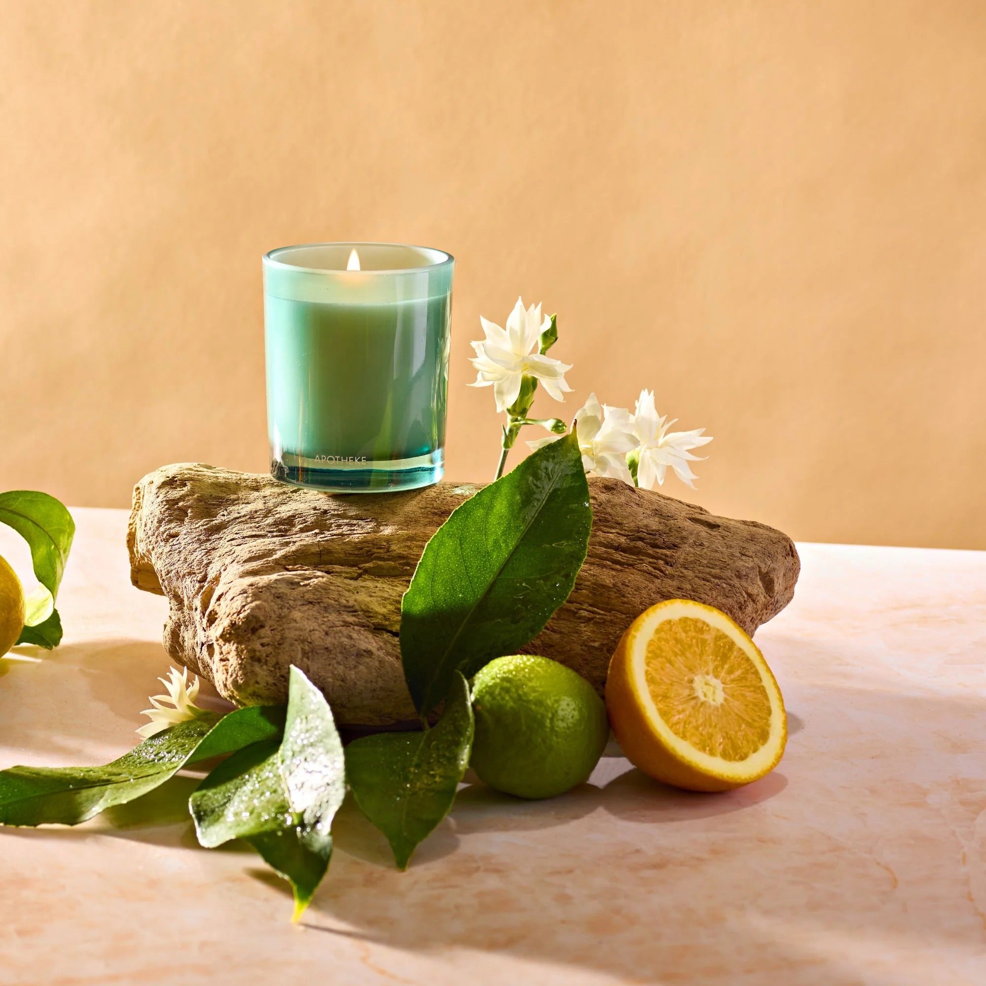 Candle in a glass holder on a rock with lemons, limes, and flowers on a beige background