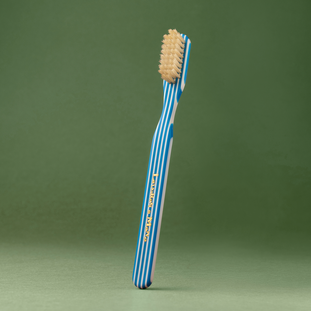 A single toothbrush with a blue and white striped handle and beige bristles, standing upright against a solid green background.