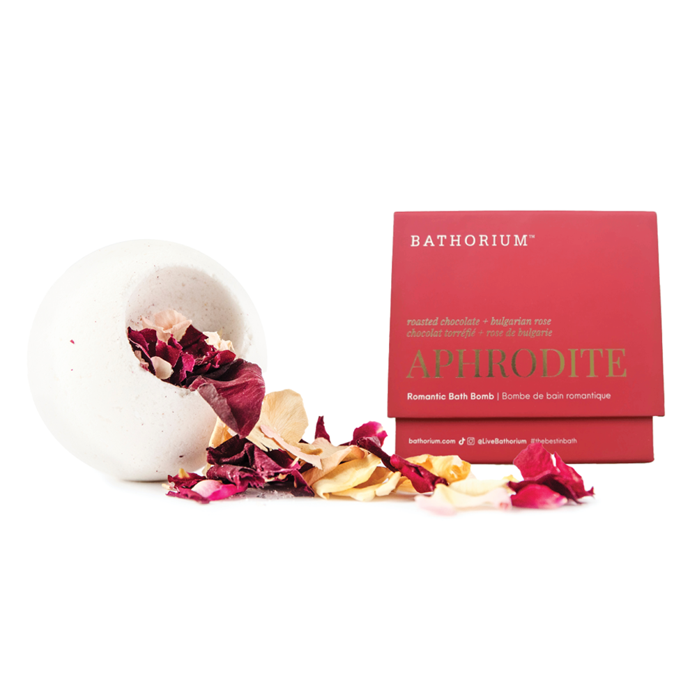 A white bath bomb with dried rose petals spilling out next to its red and gold Bathorium Aphrodite box on a white background.
