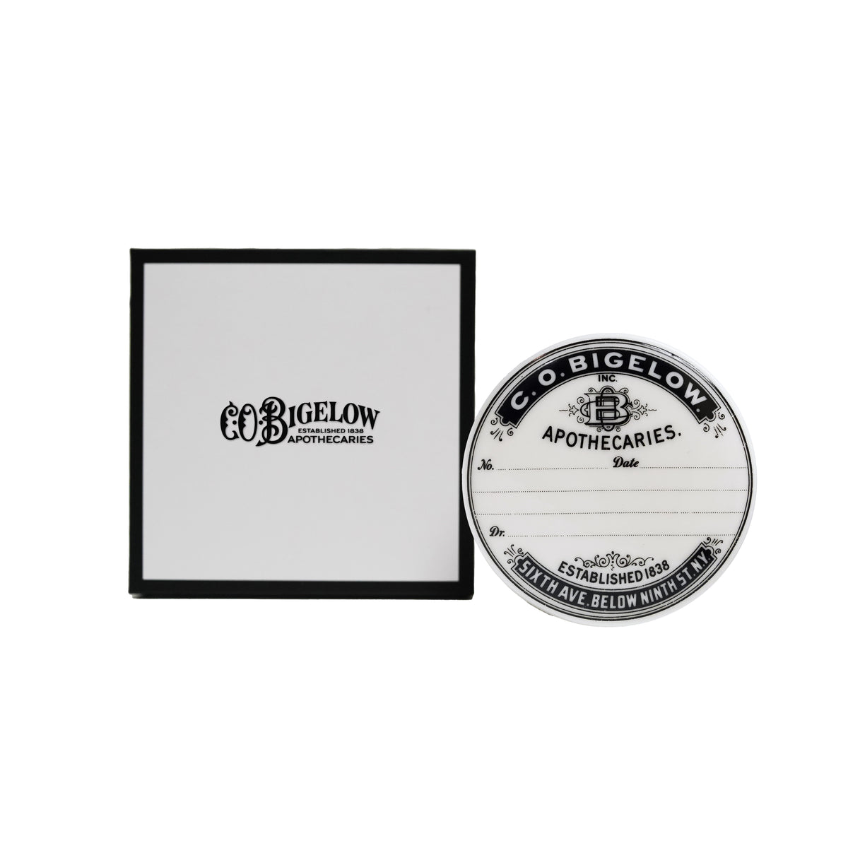A round white and black Co. Bigelow Apothecaries jar next to its black and white presentation box on a plain white background.