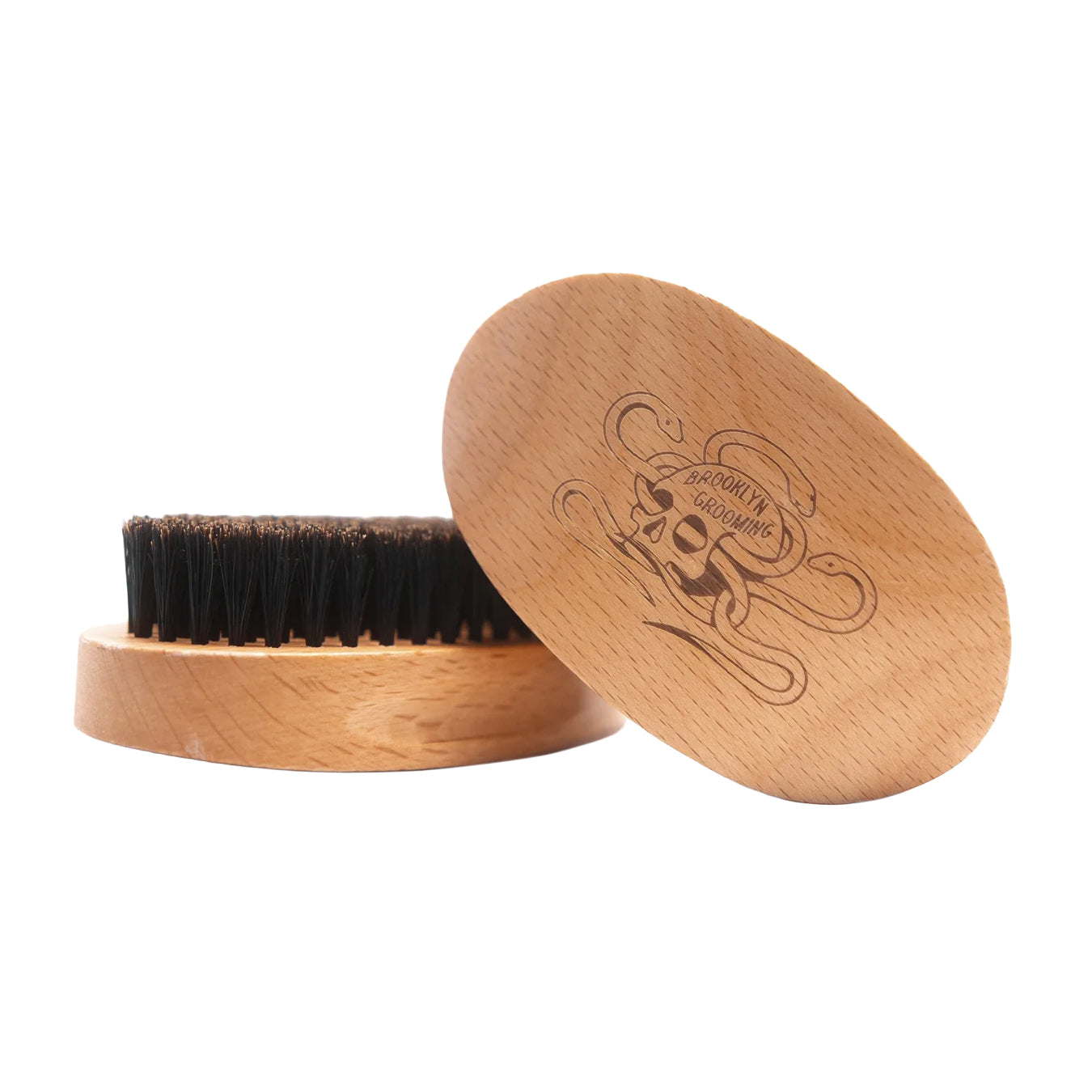 A wooden grooming brush with dark bristles and a matching oval wooden lid engraved with a skull and the brand name 'Brooklyn Grooming', shown on a white background.