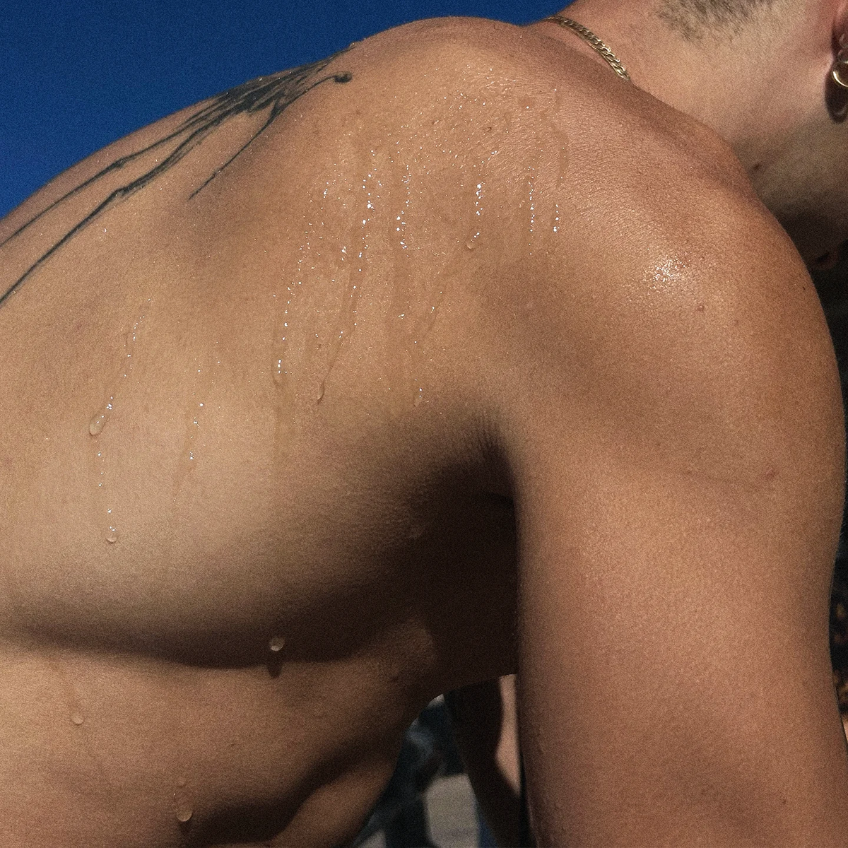 Close-up of a person's bare upper back and shoulder with visible sweat droplets under bright sunlight, against a blue sky background.