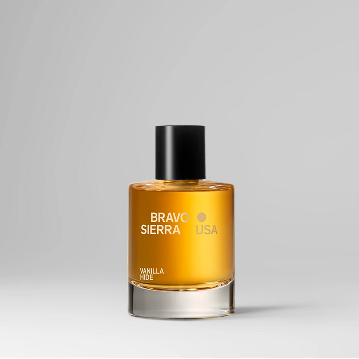 A bottle of Bravo Sierra Vanilla Hide perfume with amber-colored liquid, a black cap, and gold lettering on a light gray background.