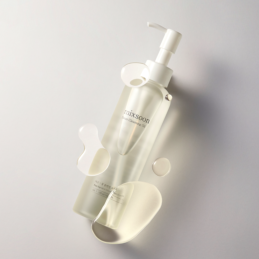 Bottle of mixsoon Bean Cleansing Oil with a white pump dispenser, shown on a light gray background with graphical translucent silicone pieces arranged around it.