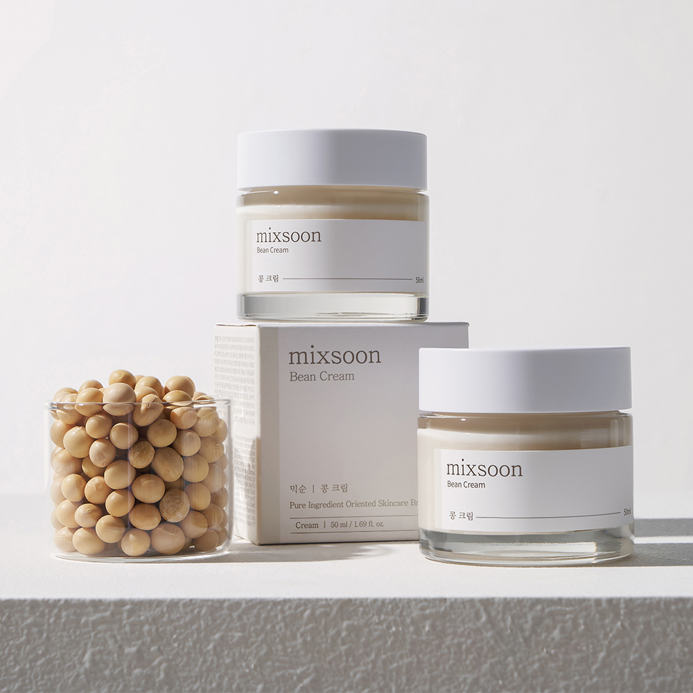 Mixsoon Bean Cream with their packaging box and a glass jar of unroasted soybeans, arranged on a light gray textured surface against a white background.