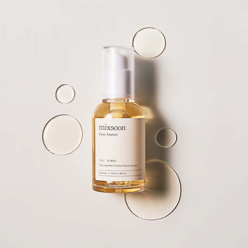A bottle of mixsoon Bean Essence skincare serum with a white pump and a beige label, set against a light gray background with decorative translucent oil pools.
