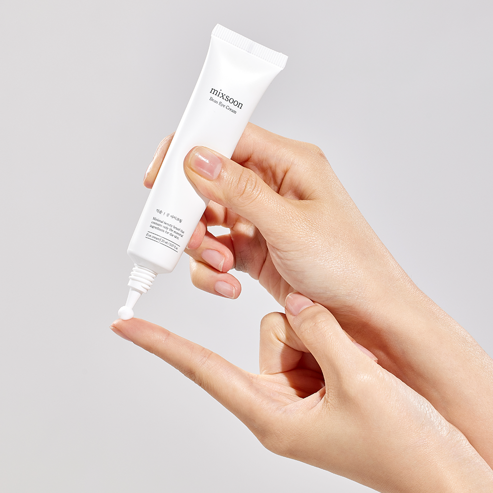 Person squeezing mixsoon Bean Eye Cream onto their finger in front of a gray background