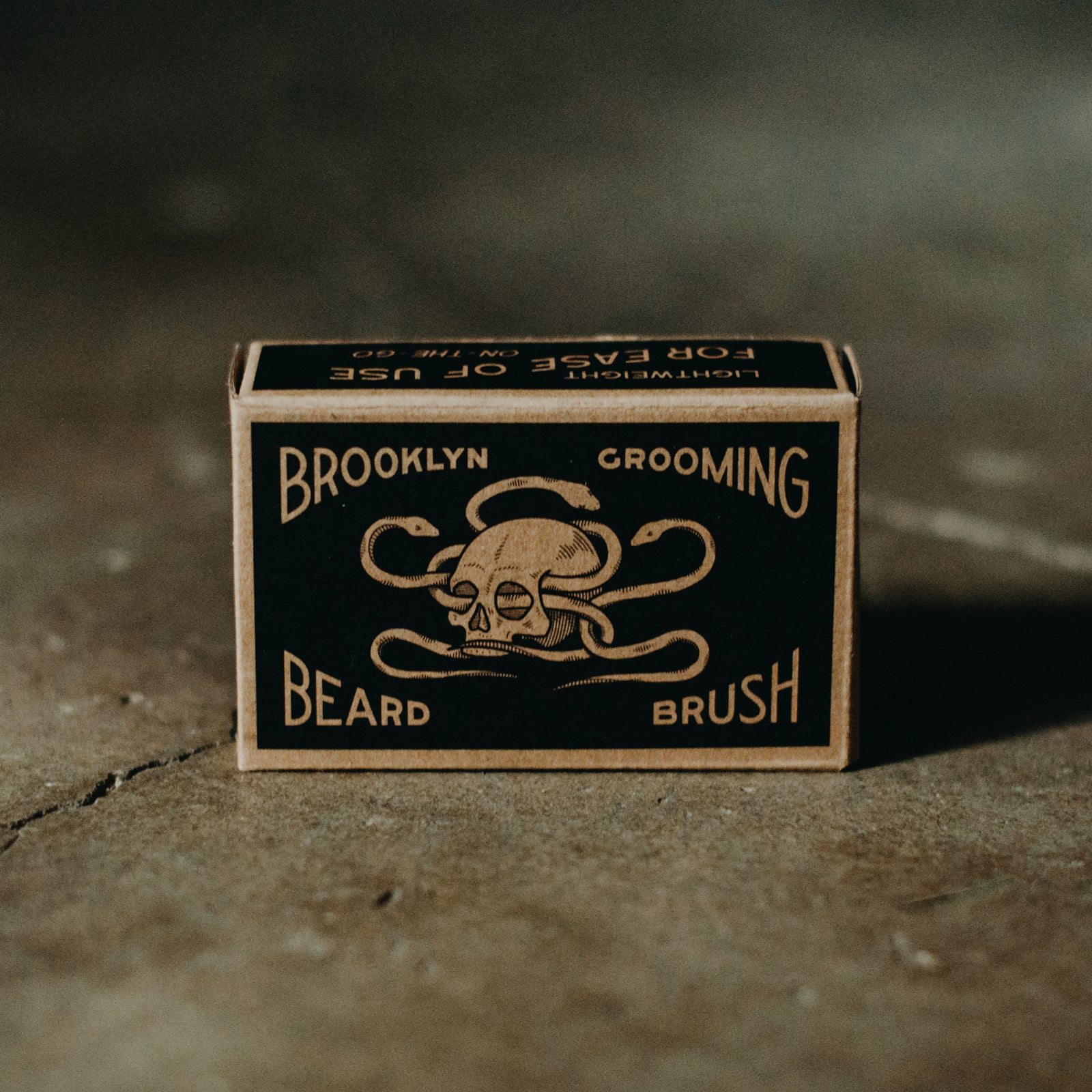 Box of Brooklyn Grooming Beard Brush with skull and snake design on a textured surface