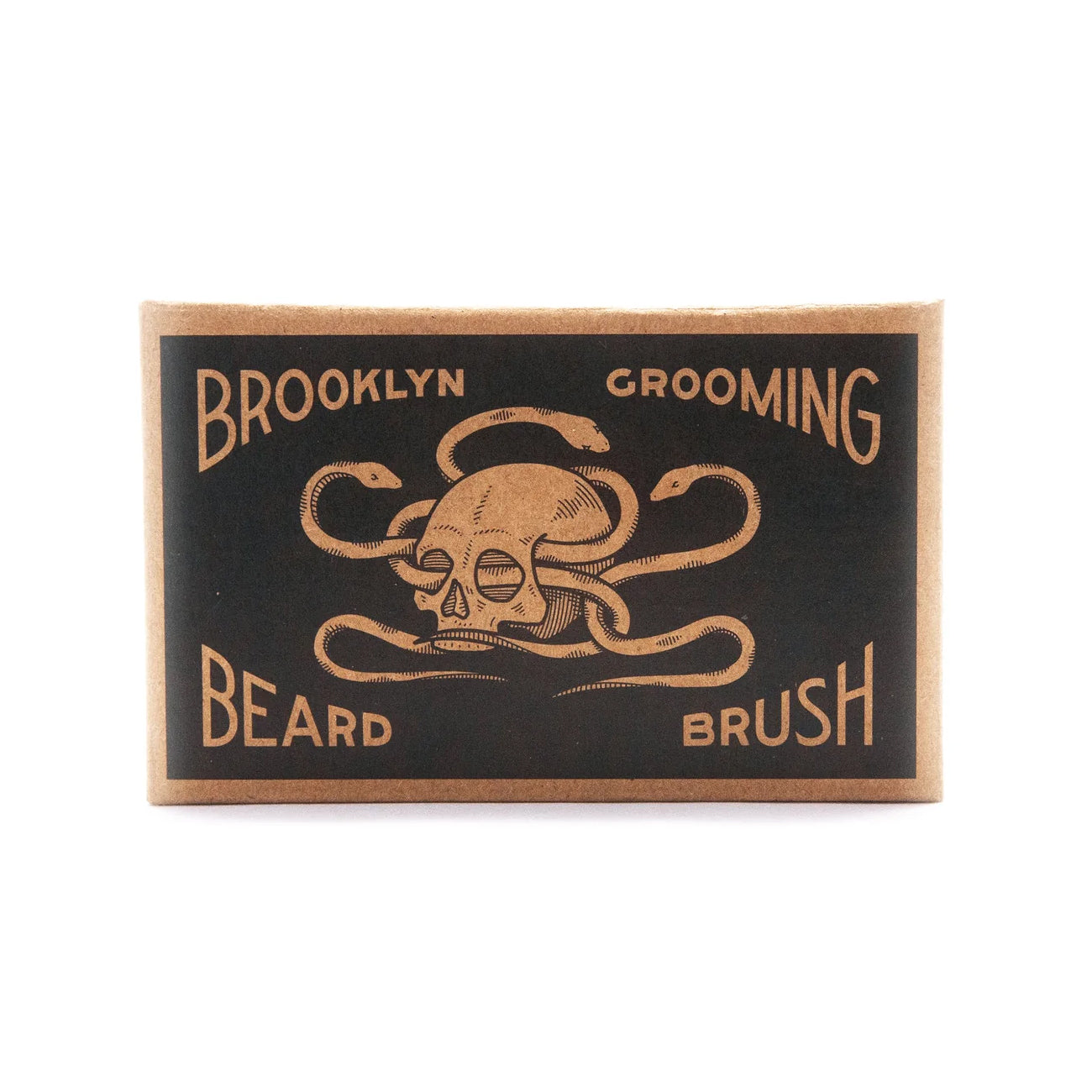 Brooklyn Grooming beard brush in a rectangular cardboard case with a black front panel and tan skull-and-snakes graphic, photographed on a white background.
