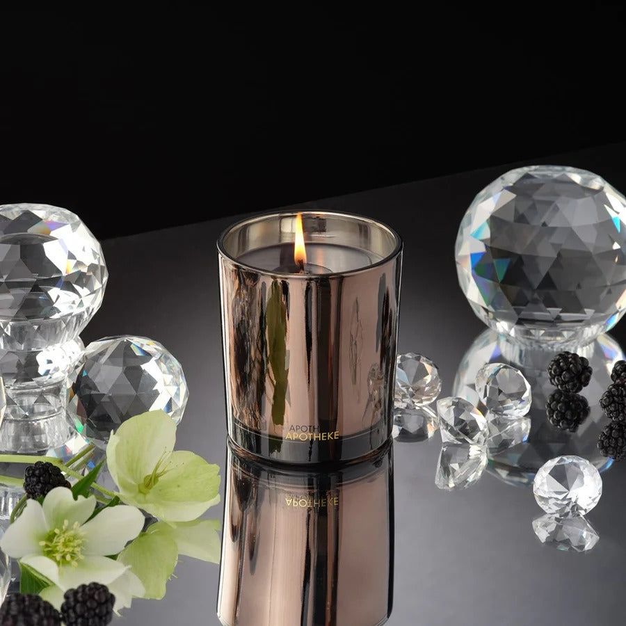 Candle in a decorative container with crystals and flowers on a reflective surface