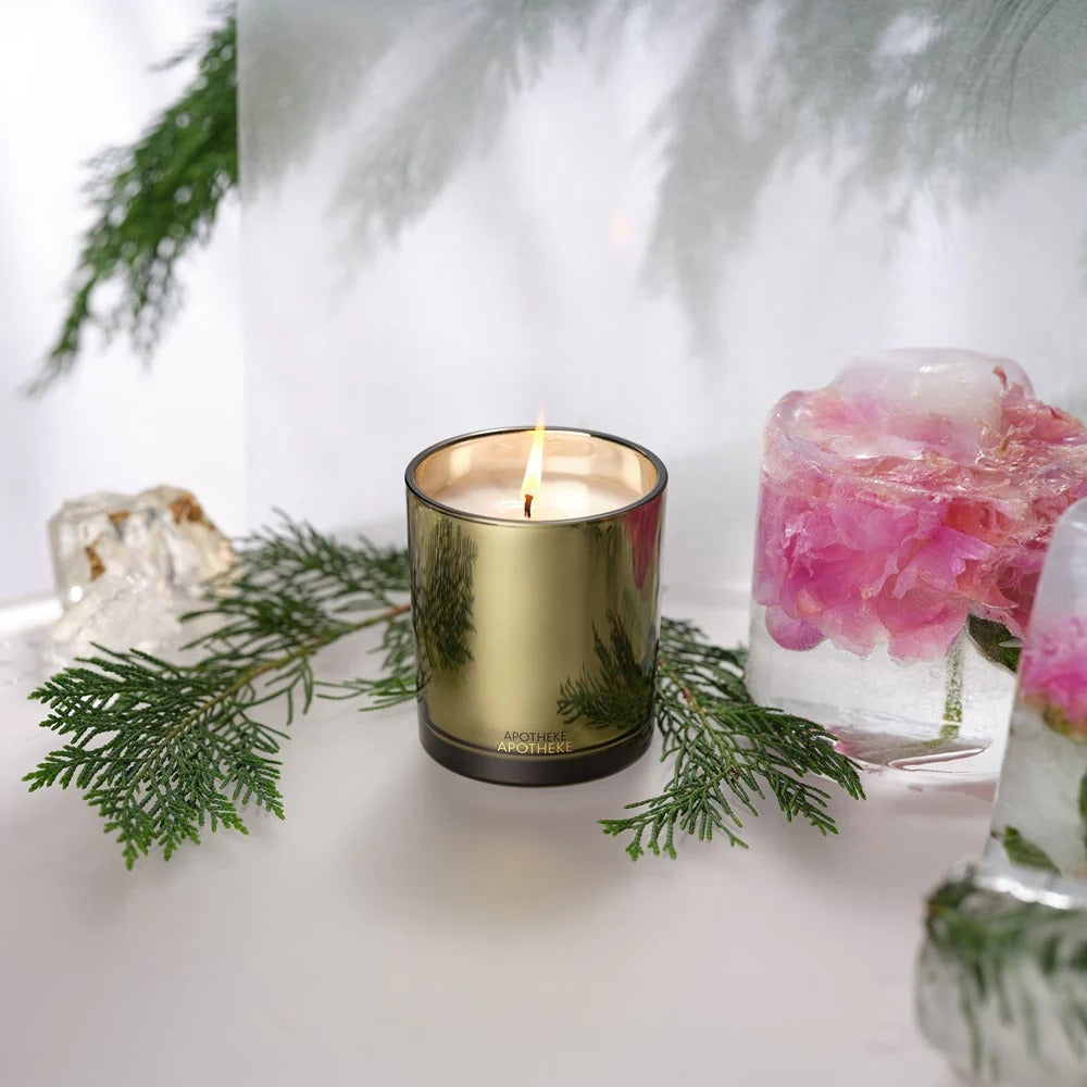 Gold candle with greenery and floral elements on a white surface