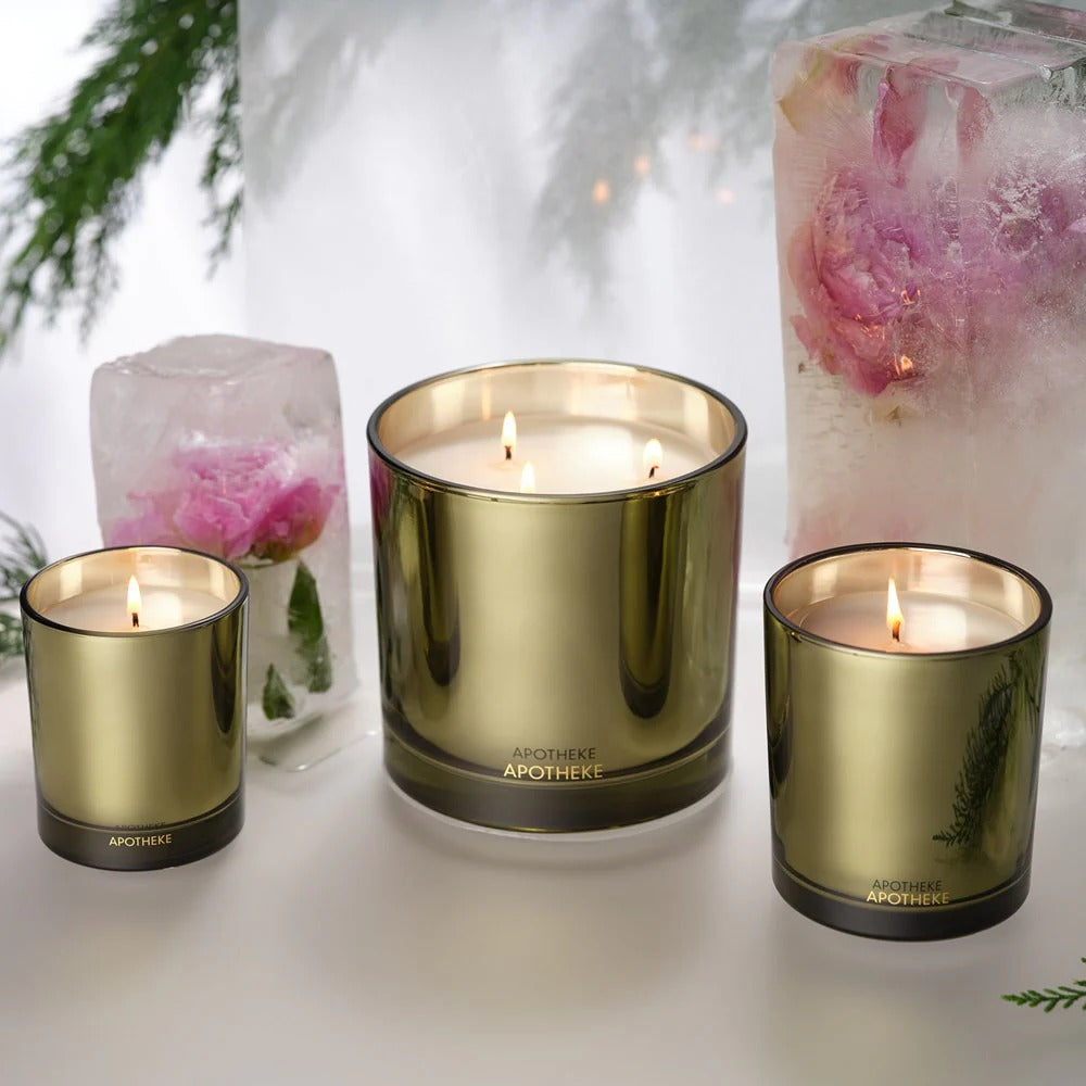Three gold-colored candles with 'Apotheke' branding on a white surface with decorative elements.