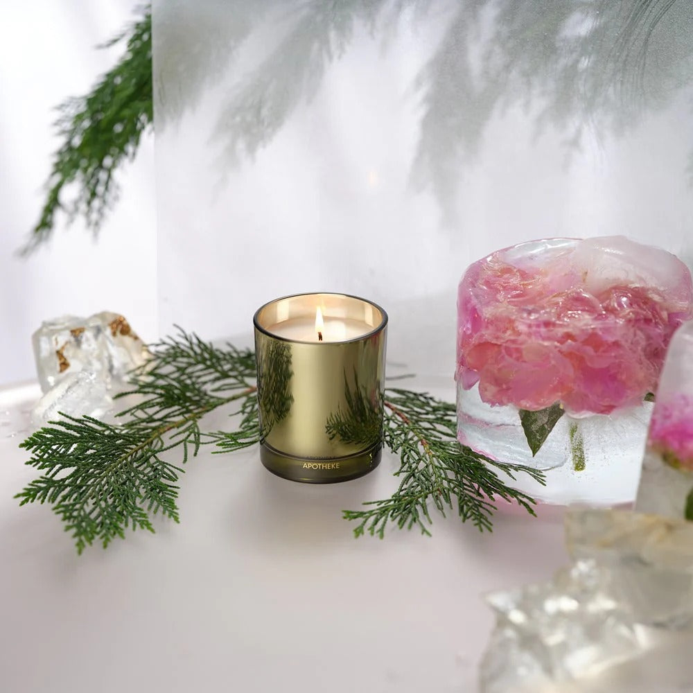 Gold candle with greenery and a pink floral arrangement in the background