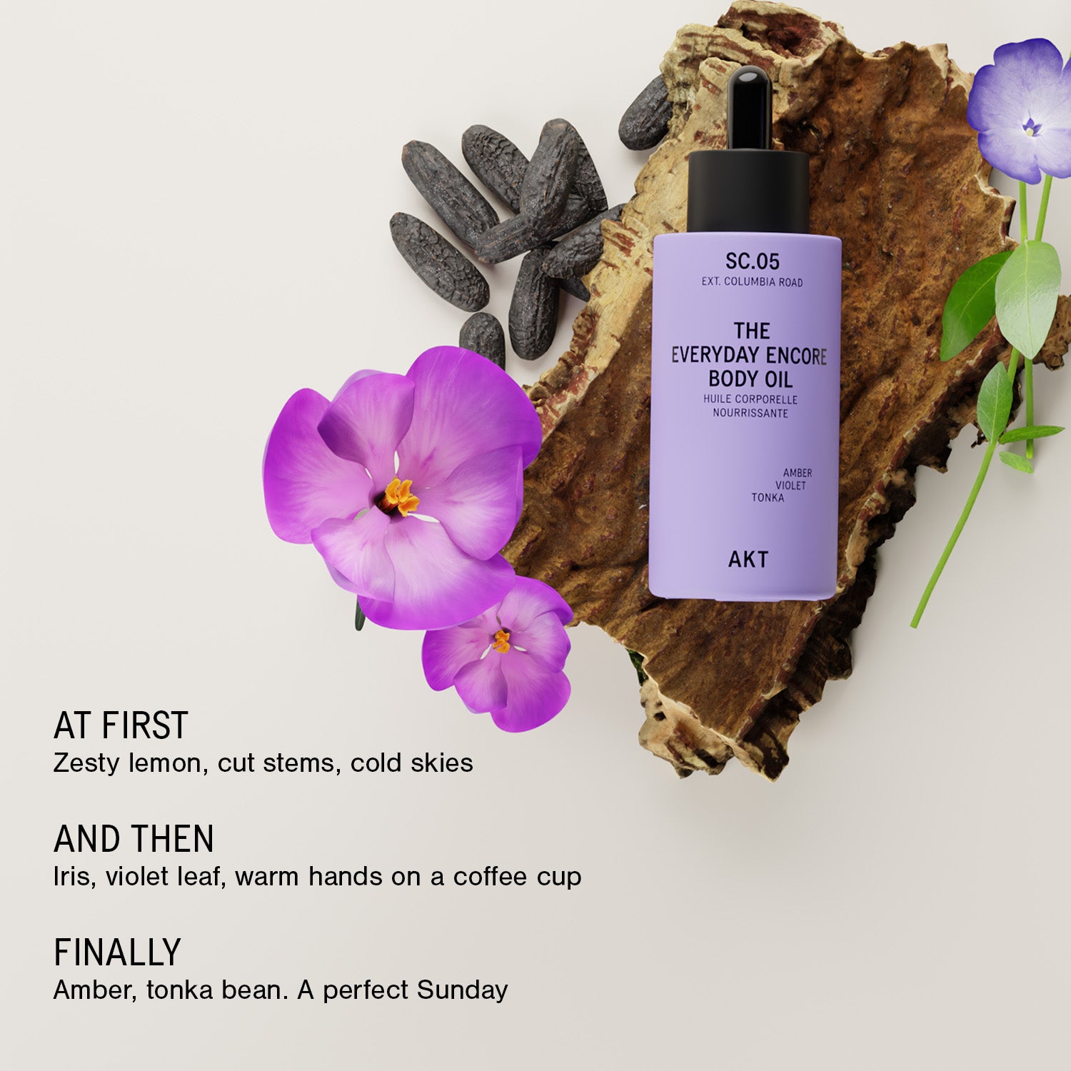 A bottle of AKT SC.05 Everyday Encore Body Oil in lavender purple with a black dropper cap, styled on a rustic wood slice with black stones and purple flowers on a light beige background with descriptive text.