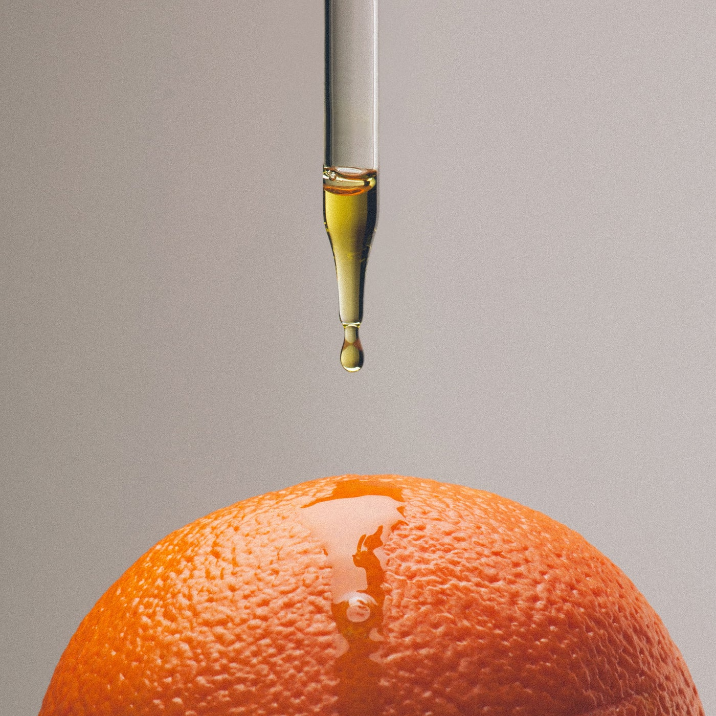 Orange with a dropper dripping oil onto it against a gray background