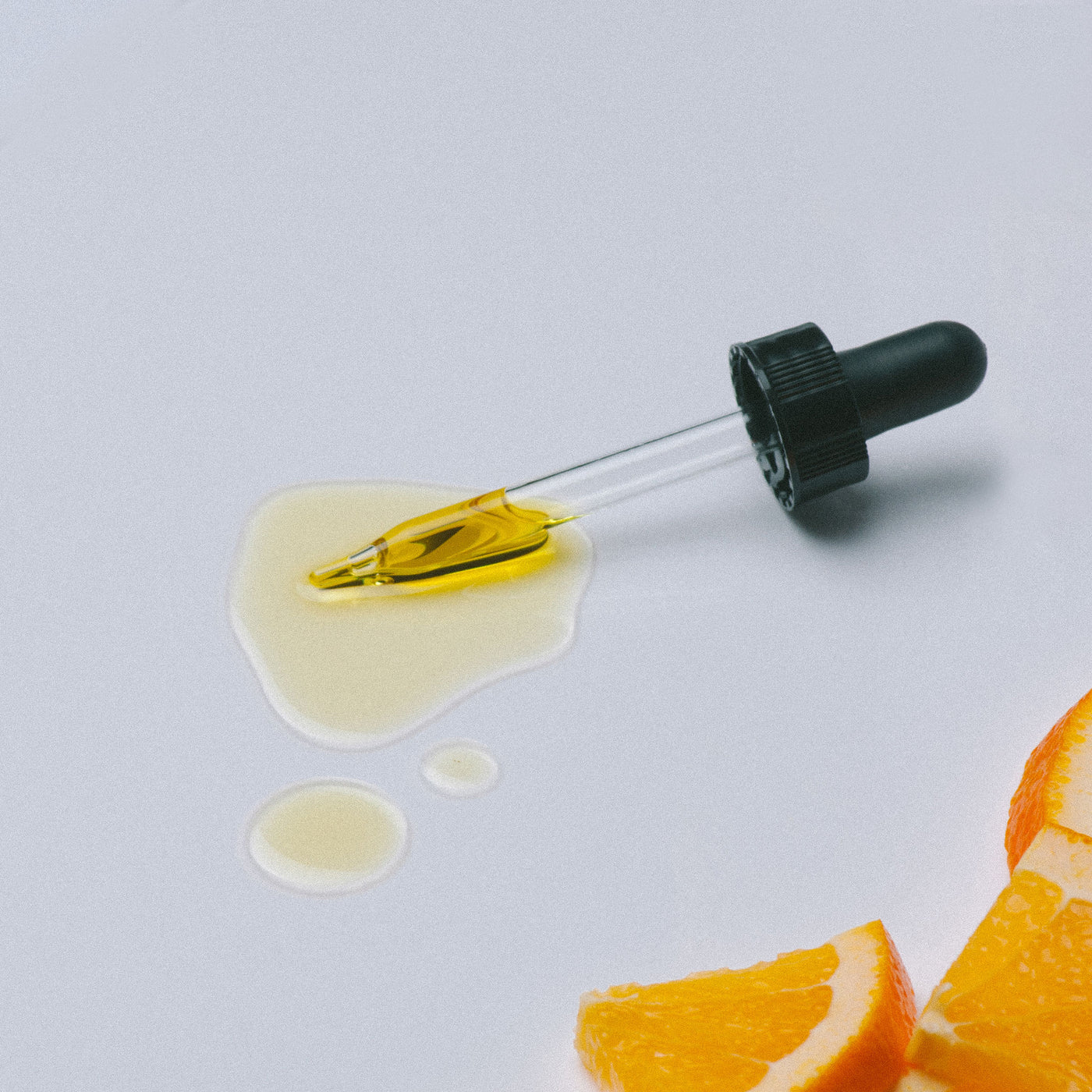 Dropper with yellow liquid next to orange slices on a light gray background