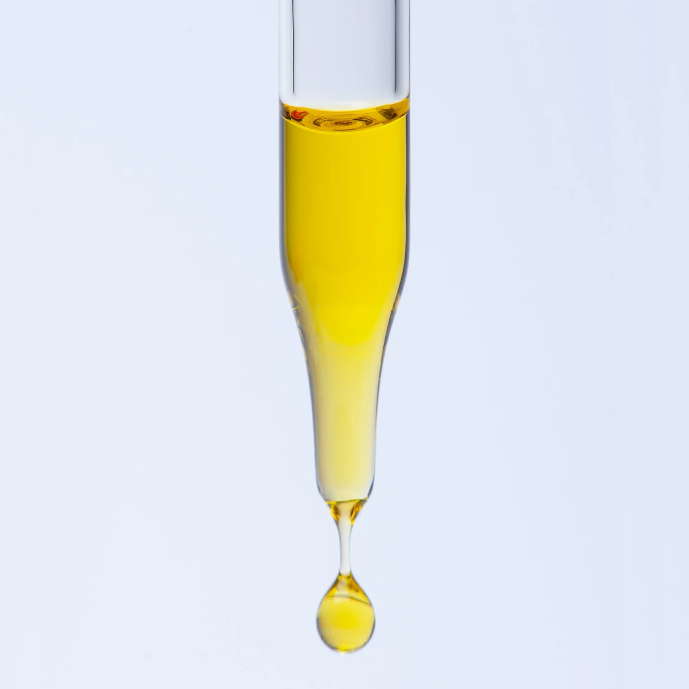 Yellow liquid dripping from a glass pipette on a light gray background