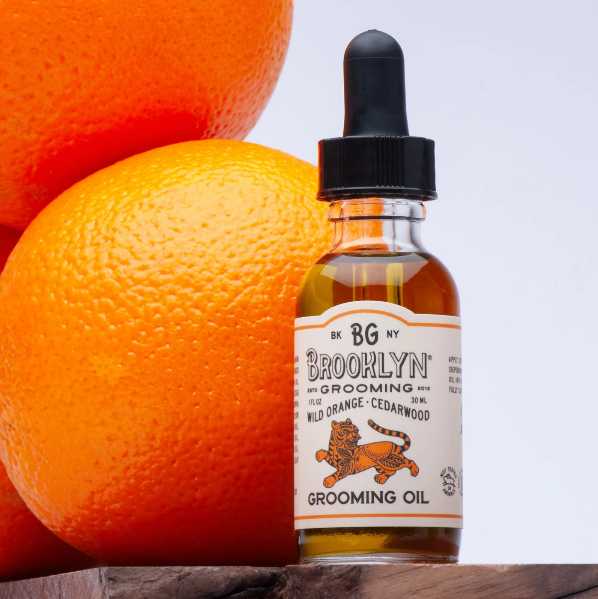 Bottle of Brooklyn Grooming Oil with oranges on a wooden surface