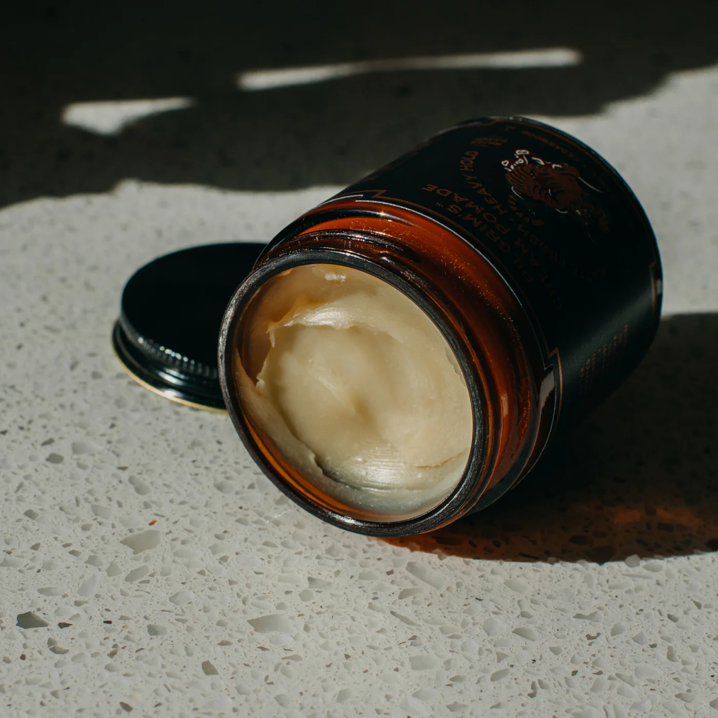 Jar of cream on a textured surface with a dark lid