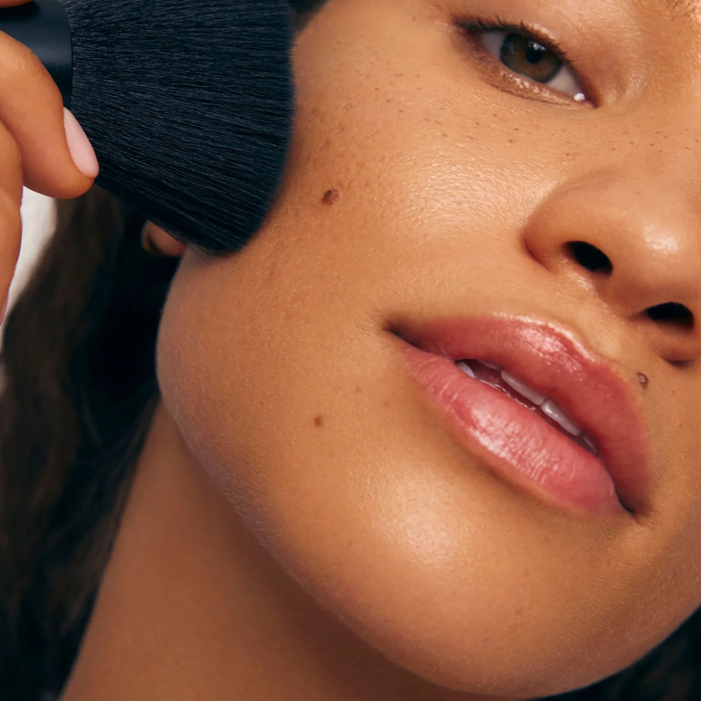 Close-up of a person applying makeup with a brush to their face.
