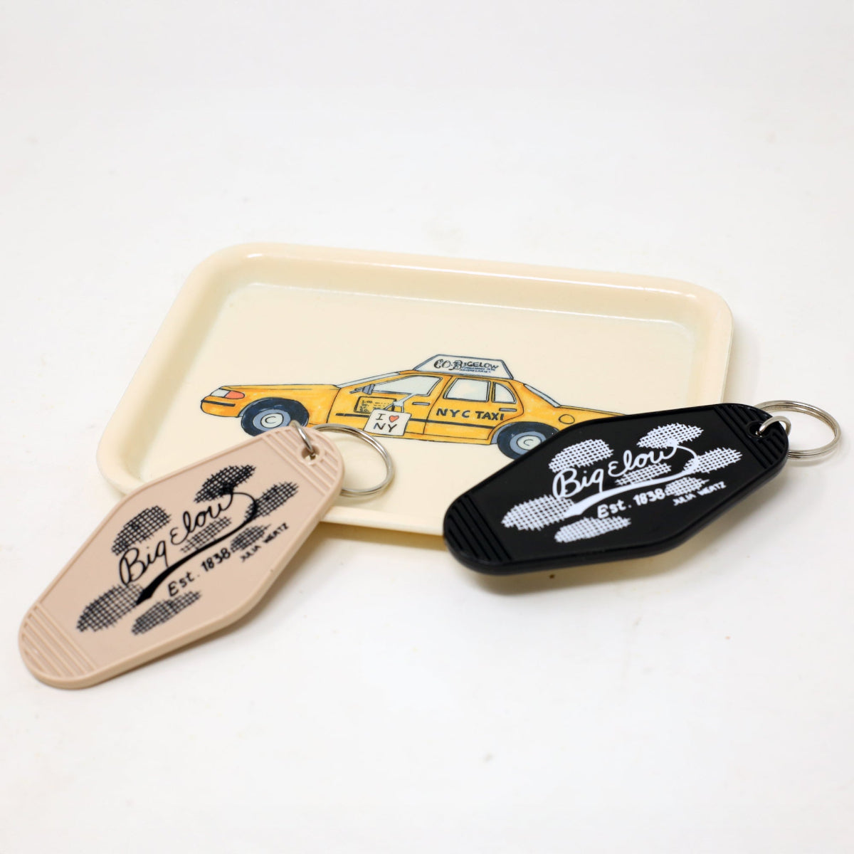 Two Bigelow Hotel keychains on a trinket tray featuring a yellow taxi illustration on a white background.