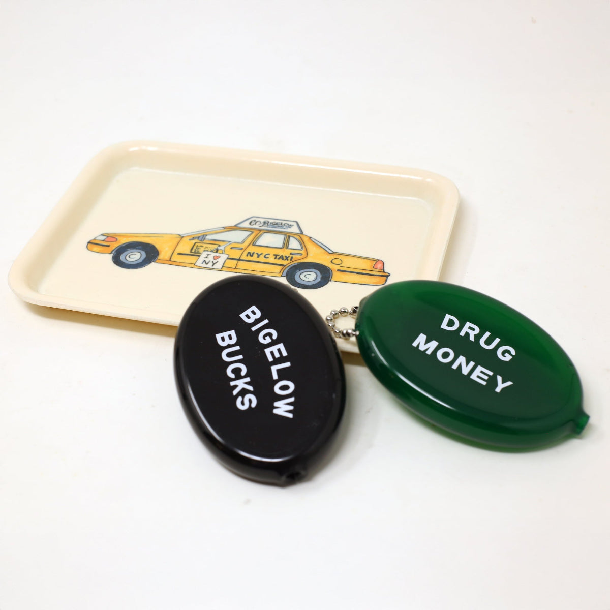 Two coin pouches labeled 'Bigelow Bucks' and 'Drug Money' on a trinket tray with a yellow taxi illustration.