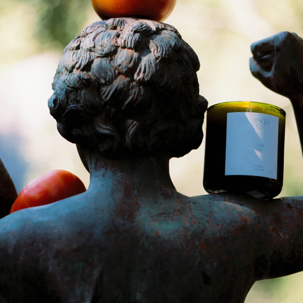 Statue holding Flamingo Estate Heirloom Tomato candle  on a blurred background