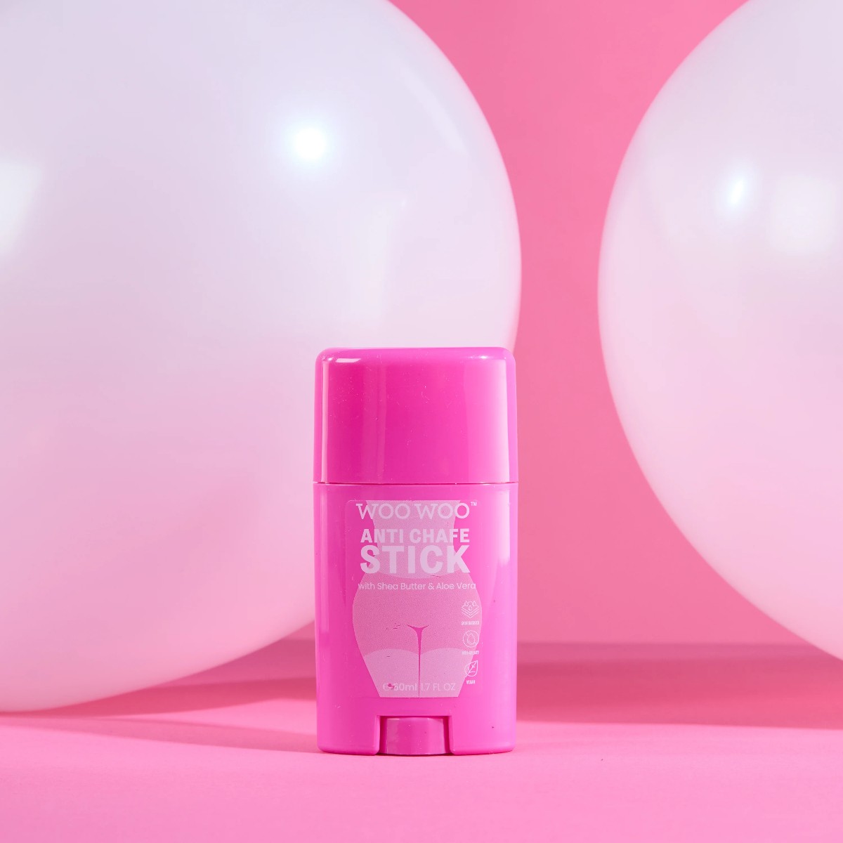 A pink stick-shaped product labeled 'WOO WOO ANTI CHAFE STICK' stands centered on a pink surface with large white balloons in the background.