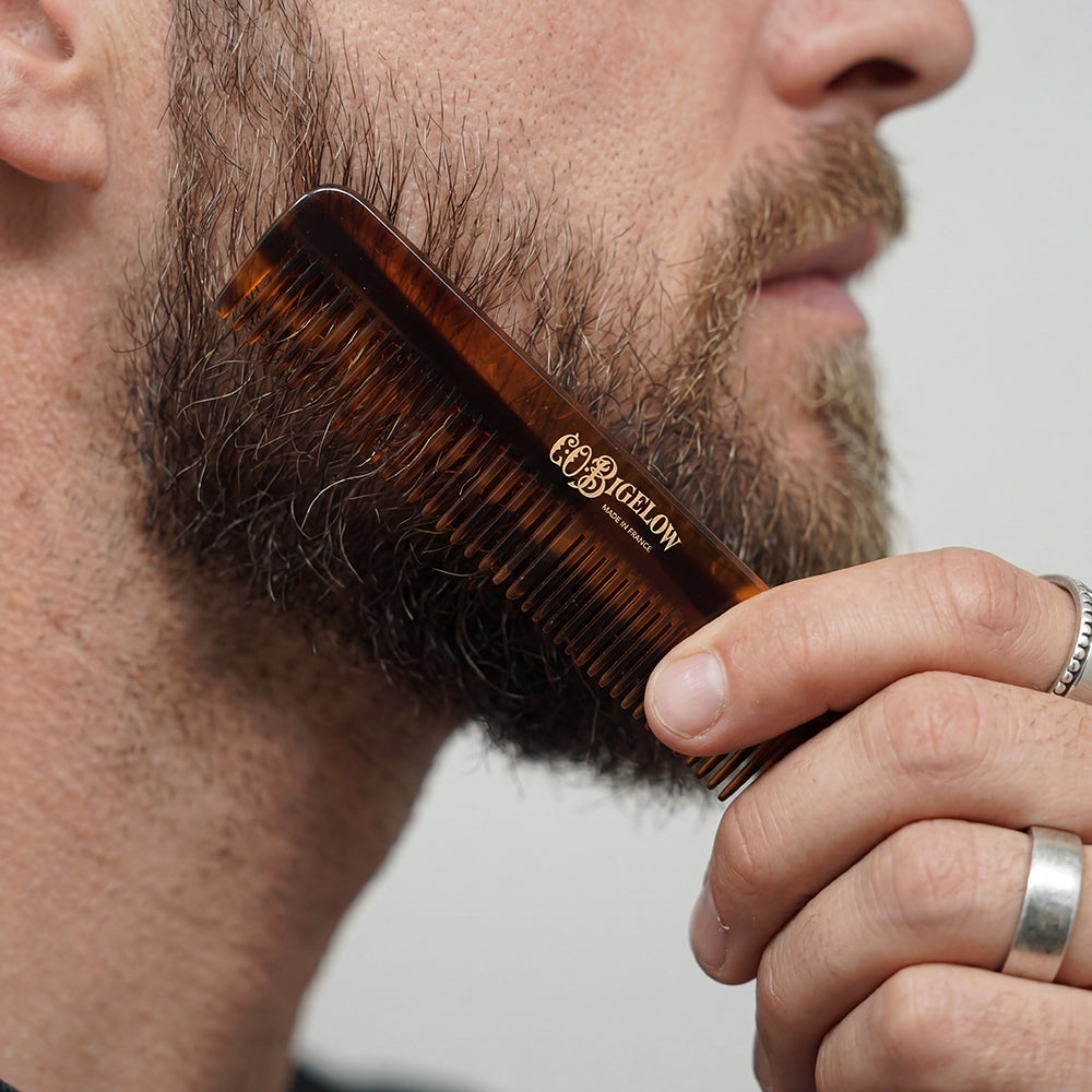 Man grooming his beard with a brown comb featuring 'C.O. Bigelow' branding.