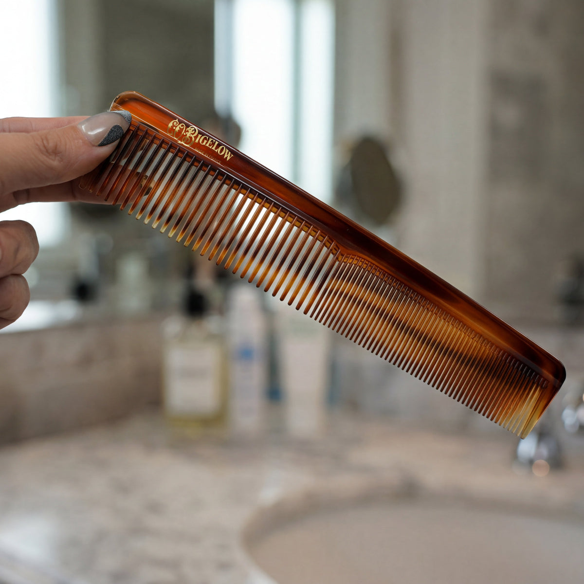 Person holding C.O. Bigelow Detangling Comb in front of bathroom sink.