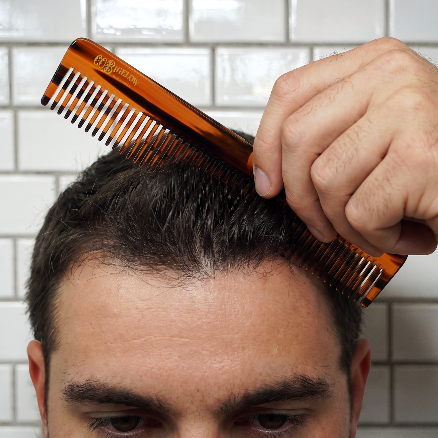 Person combing hair with a tortoiseshell comb against a tiled wall background
