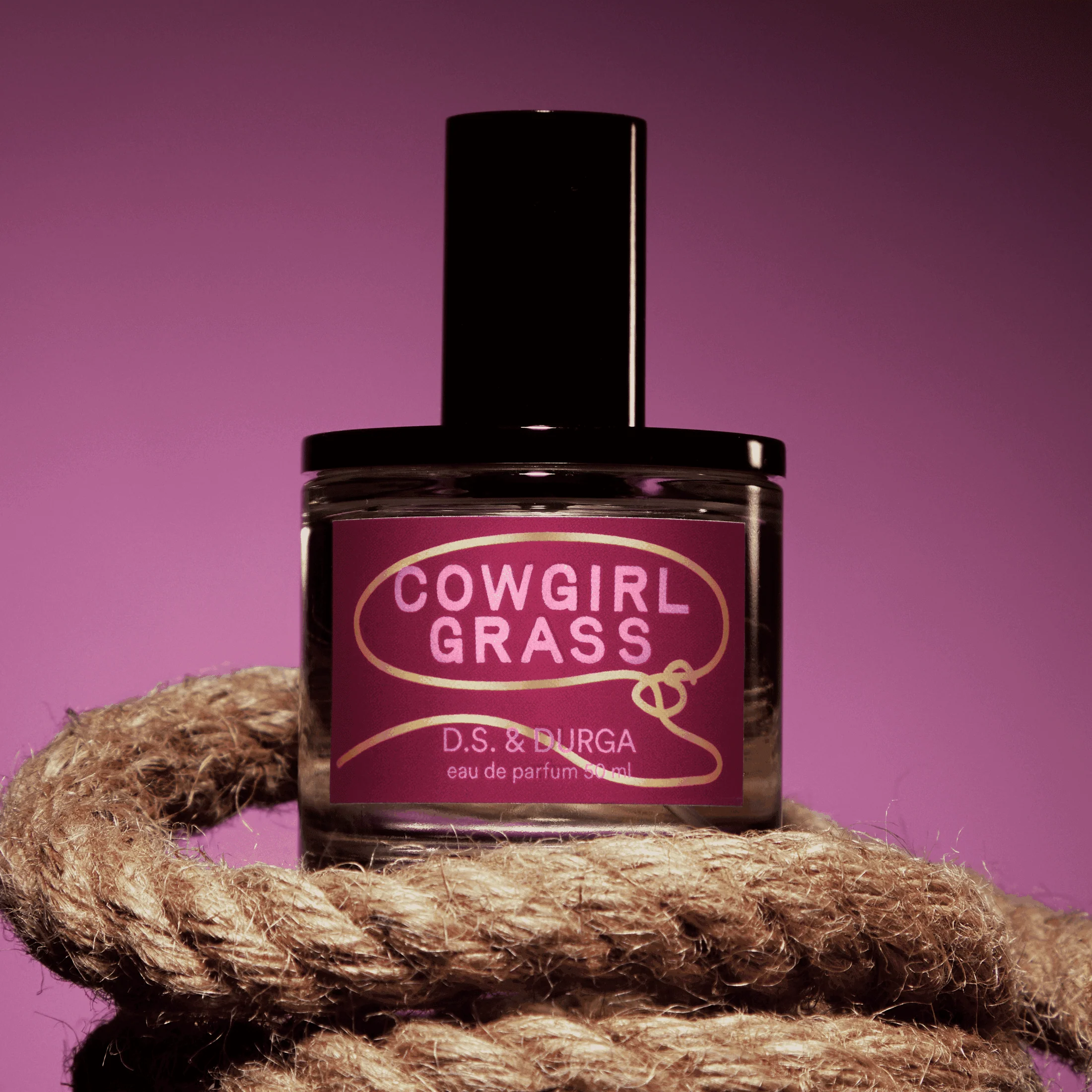 Cowgirl Grass Eau de Parfum on top of a rope in front of a pink background.