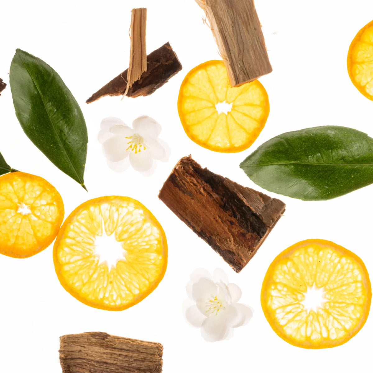 A styled flat-lay of citrus ingredients and natural elements on a white background, including bright yellow citrus slice halves, green leaves, small white blossoms, and pieces of brown bark or wood.