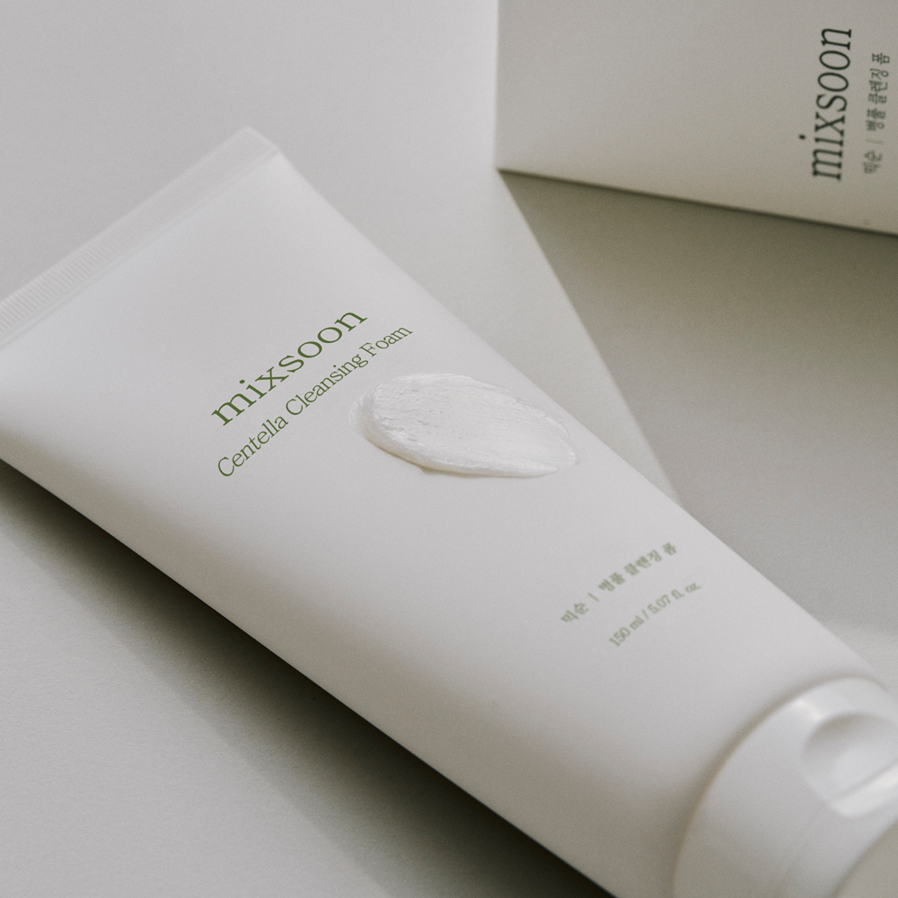 A white squeeze tube of Mixsoon Centella Cleansing Foam with a dollop of white foam on the front, photographed on a clean light gray surface with a matching box in the background.