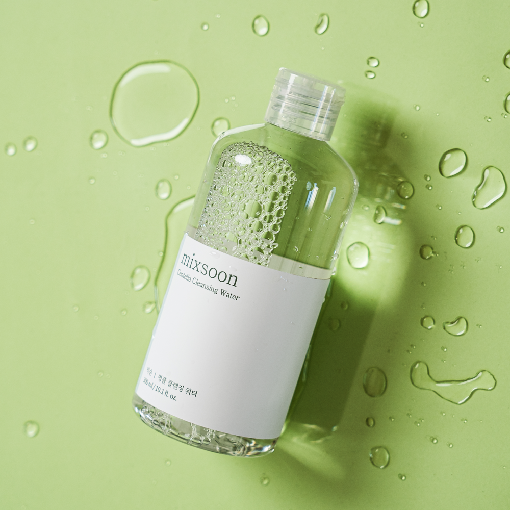 Bottle of mixsoon Centella Cleansing Water on a green background with water droplets.
