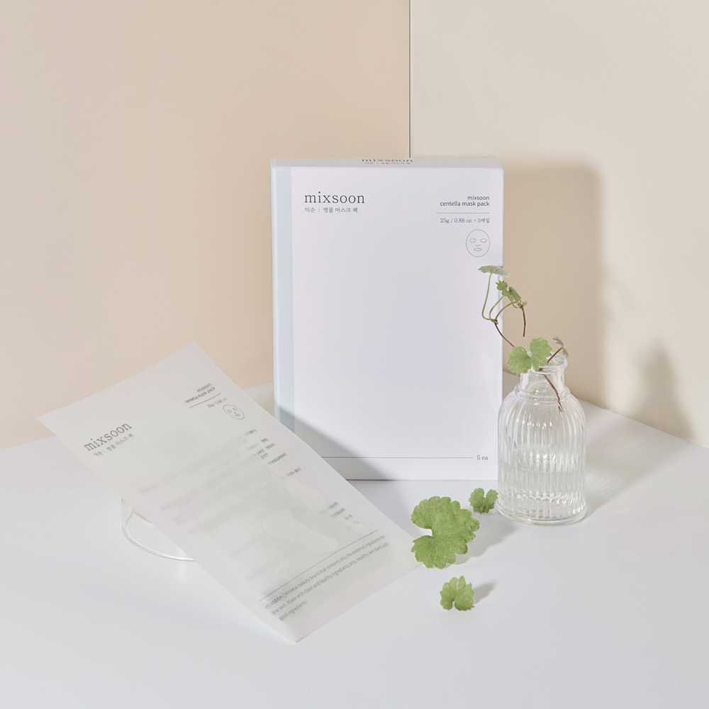A white box of Centella Mask Pack sits on a white surface next to a clear ribbed glass vase with green leaves